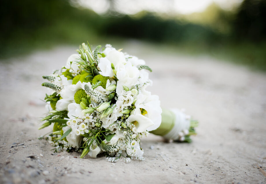 A bouquet of white and green flowers lies on a sandy ground, displaying a mix of blooms and green foliage.