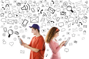 Two people using tablets back-to-back with digital communication icons, such as emails and social media symbols, floating above them.