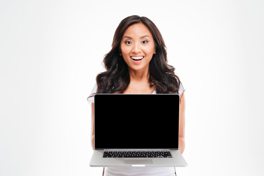 A woman smiling while holding an open laptop with a blank screen.