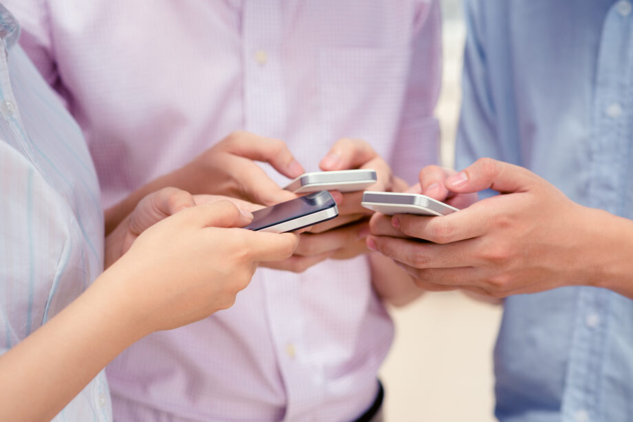 Three people standing close together, each focused on their smartphone screens.