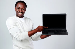 Man smiling and pointing at a blank laptop screen while holding it with one hand.