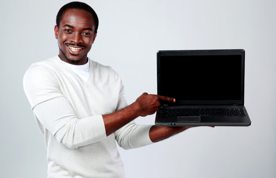 Man smiling and pointing at a blank laptop screen while holding it with one hand.