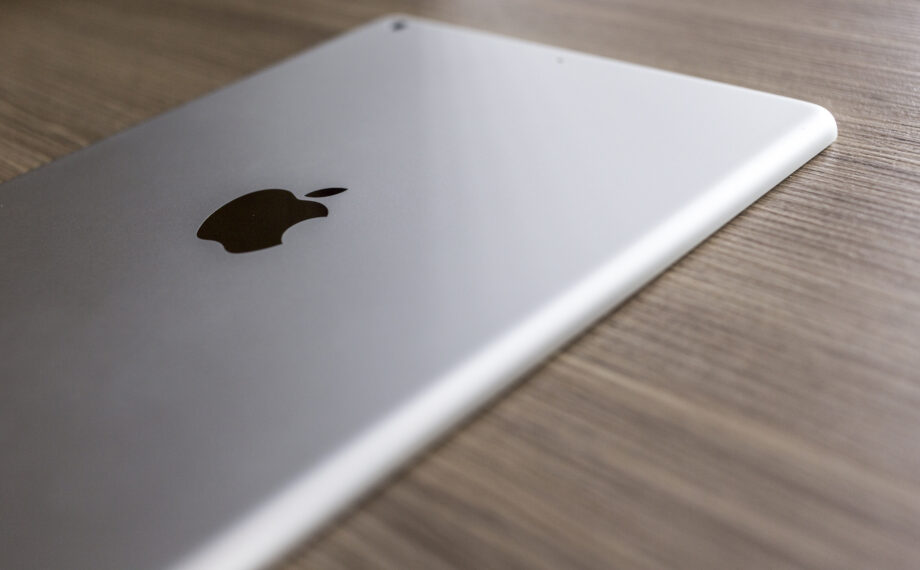 A close-up of a silver tablet with the Apple logo, placed on a wooden surface.